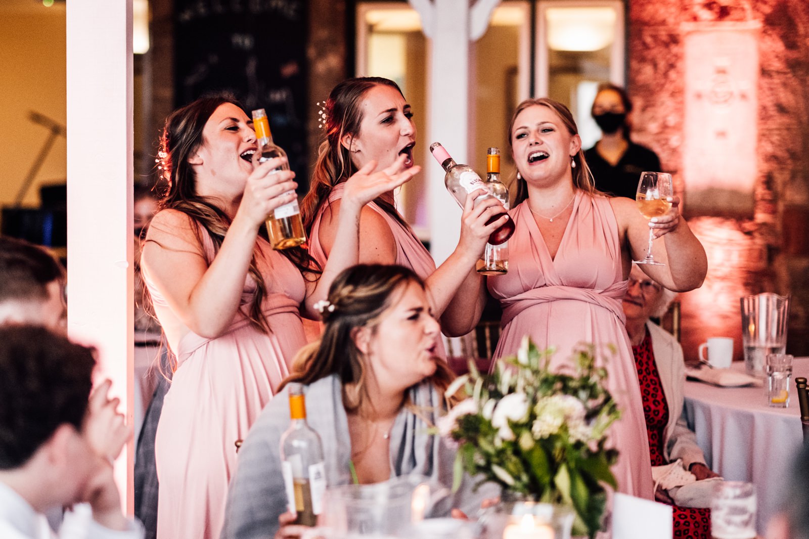 Bridesmaids sining into wine bottles