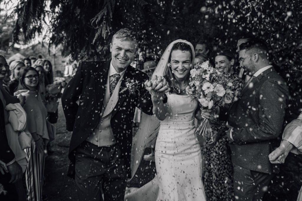 Bride and groom laughing as they walk through a cloud of confetti at their South Wales wedding