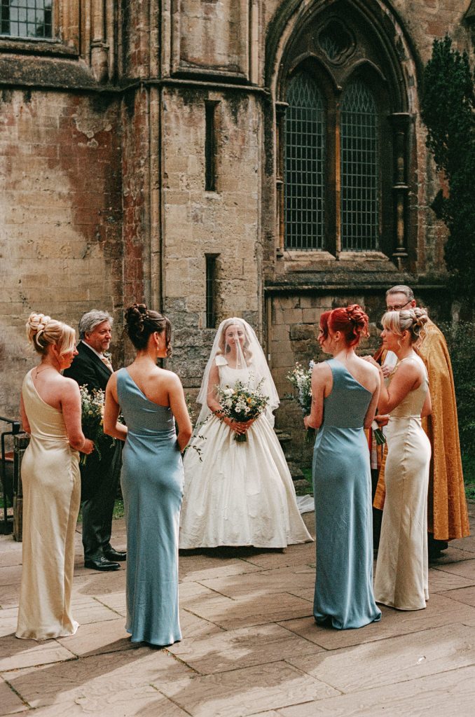 35mm analogue film photograph of bride waiting outside Llandaff Cathedral in Cardiff, South Wales with bridesmaids.