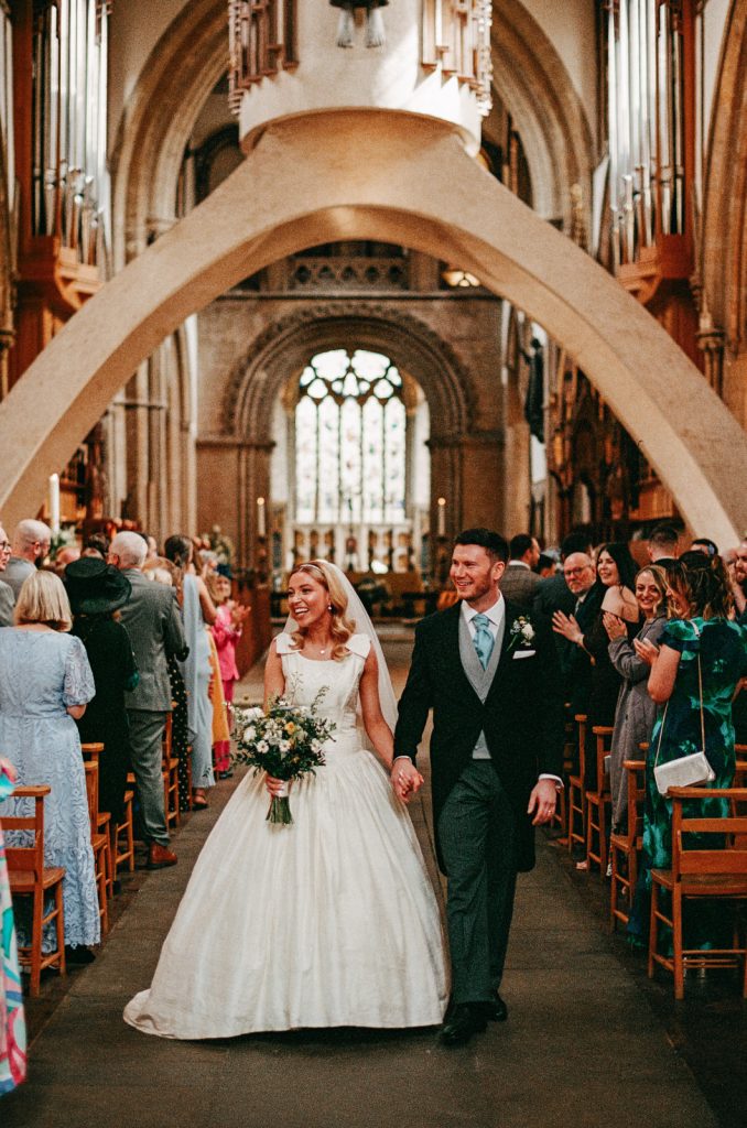 35mm analogue film photograph of bride and groom walking down the aisle of Llandaff Cathedral in Cardiff, South Wales.